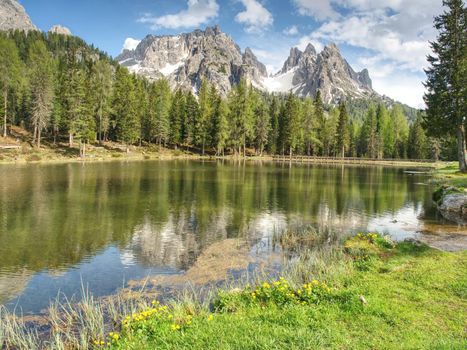 The calm blue lake between the sharp rocks. Mountain peaks touching to dramatic sky with clouds. Wonderful valley. Hiking and Tourism Concept