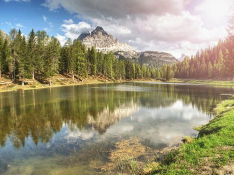 The calm blue lake between the sharp rocks. Mountain peaks touching to dramatic sky with clouds. Wonderful valley. Hiking and Tourism Concept