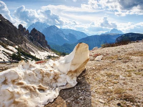 The rest of melting snow at gravel road in spring Alps mountains. View to blue far peaks.