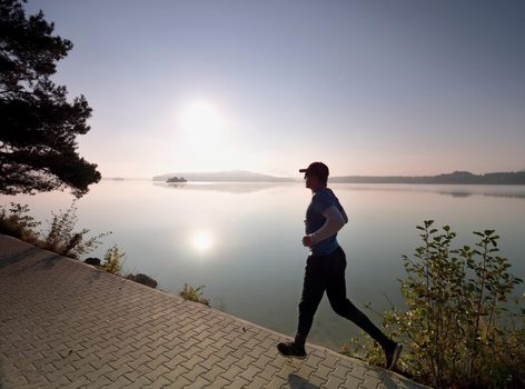 Freeze sportsman in  running pose.  Runner is sprinting along mountain lake within morning moody atmosphere.