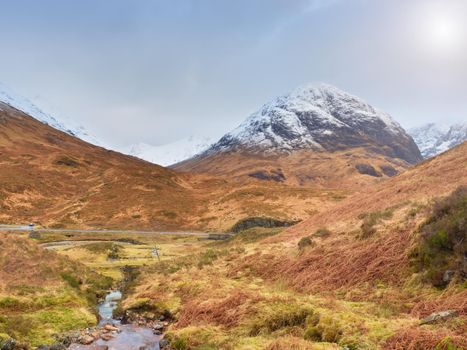 Mountains landscape wild stream in front. White snowy mountain peaks and grey cloudy sky