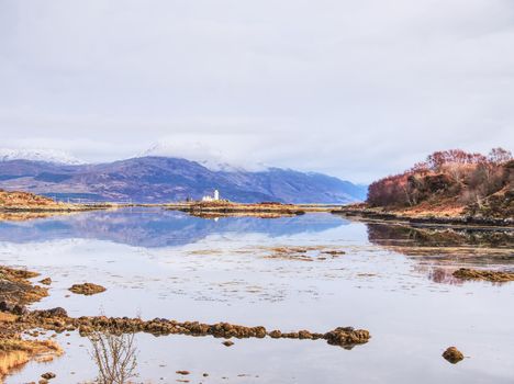 Isle Ornsay with white tower of Lighthouse; Isle of Skye; Scotland. Sunny winter day with snowy mountains in background.