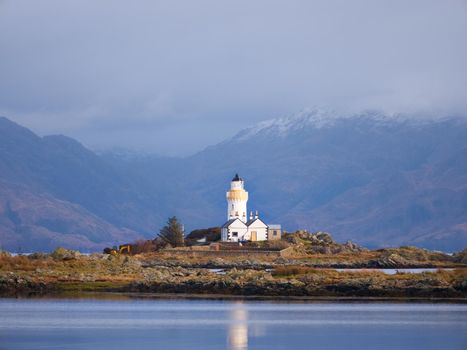 Isle Ornsay with white tower of Lighthouse; Isle of Skye; Scotland. Sunny winter day with snowy mountains in background.