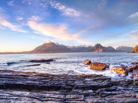 Peaceful dawn at Elgol bay. Low angle  overlooking of offshore rocks and smooth sea, mountains at horizon. Winter  Isle of Skye, Scotland 