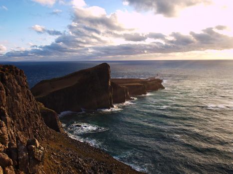 Famous view to Neist Point lighthouse on the end of  world. Foamy evening blue sea strikes against the sharp cliff.  The Isle of Skye, Scotland