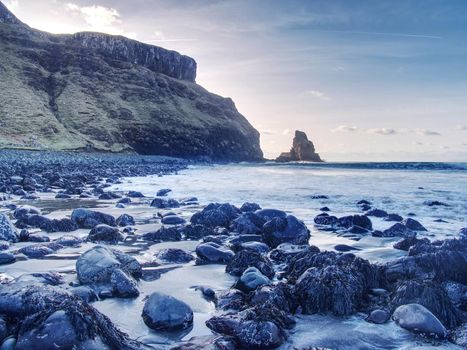 Amazing sunset, Talisker bay on the Isle of Skye in Scotland. Foamy sea, boulders and large cracked rocks with erosion marks. Rocky coastline with sea water