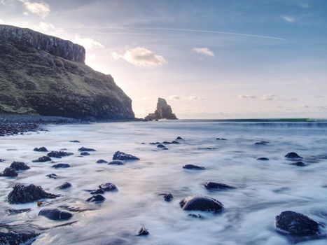 Sea stack sharp silhouette by sunset sky. Evening light on the rocks, boulders and cliff face of Talisker Bay, Isle of Skye