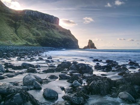 Beautifully shaped black boulders and a dramatic fiery sunset and a stony beach