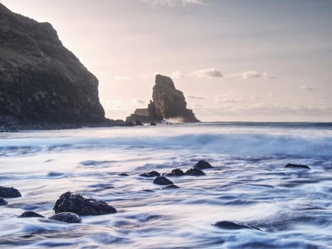 Evening Bay. Sharp rocks, black rounded boulders, stony beach, sand and dark sky.