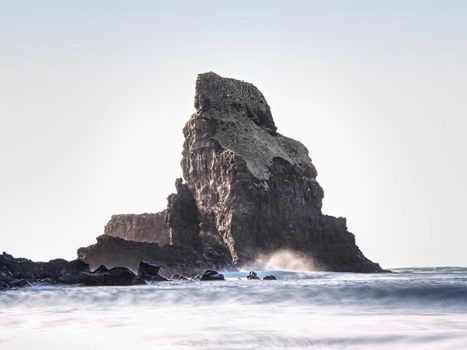 Sharp silhouette of a cliff against the background of sunset. Sea waves break on the rocks. Talisker bay, Scotland. 