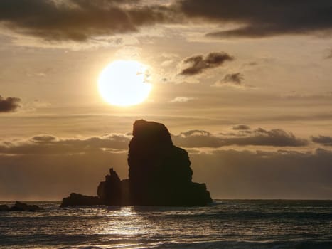 Sharp silhouette of a cliff against the background of sunset. Sea waves break on the rocks. Talisker bay, Scotland. 