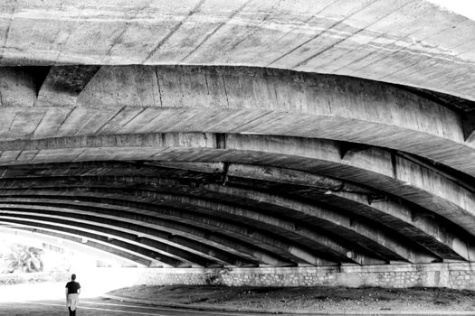 Person walking under Cement structure of a bridge in Valencia, Spain. Monochrome picture