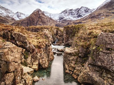 Pools and waterfalls within cloudy day in Scotland. Cold water falling from steps of sharp giant rocks