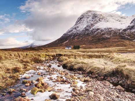 River at base of snowy mountains in Scottish Highlands near Glencoe  in winter. Cold windless winter morning