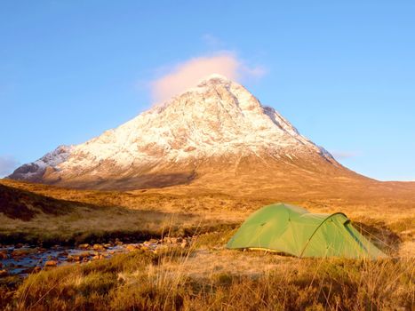 Green tent and snowy mountain peak. Higland in Scotland an marvelous sunny winter day. Dry grass and heather bushes. Hikers tent