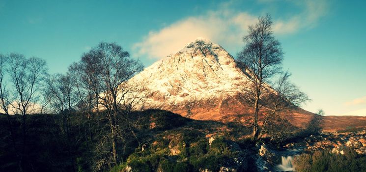 Higland in Scotland. Marvelous day  at frozen river Coupall at delta to river Etive. Snowy cone of mountain Stob Dearg 1021 metres high. Dry grass and heather bushes on banks. 