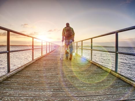 Traveler on wooden pier or jetty waiting for ferry boat. Orange and  blue lake sunset and clear sky reflection on water.