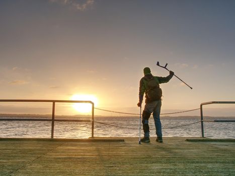 Traveler with backpack walk dificult with medicine poles.  Young tourist on bridge  near sea at the sunset