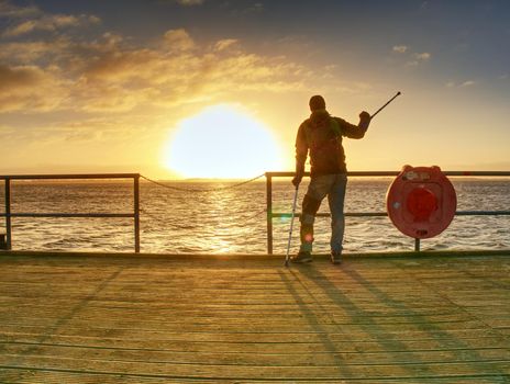 Tourist on ferry boat mole within sunrise or sunset. Warm colors, reflection of Sun in camera lens. 