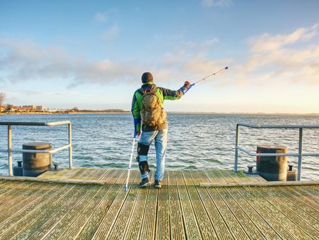 Man with a crutches on mole pier. Tourist with broken leg on crutches. Traveler with hurt leg in bandages. Full length of man with broken leg.