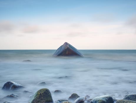 Romantic morning at sea. Big boulders sticking out from smooth wavy sea. Pink horizon with first hot sun rays. Vintage Style effect