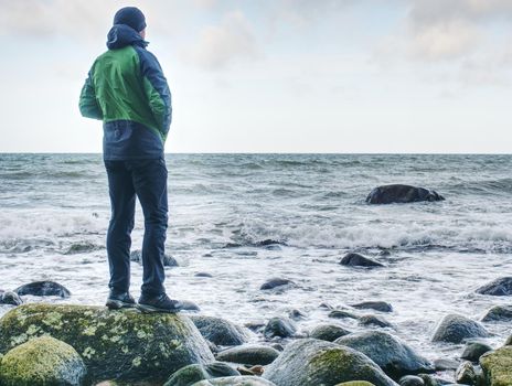 Man standing on rock in the middle of ocean.  Tourist stand alone on a rock and watching sea horizon within sunset