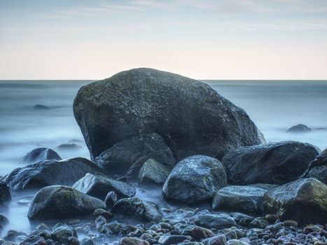 Moody seascape - storm on the sea, turquoise waves breaking on coastal cliffs against cloudy sky. Rocks at water. 