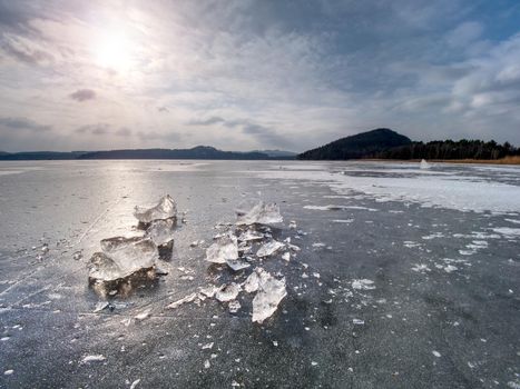 Broken pieces of thick ice over frozen lake shine in evening sun. 
