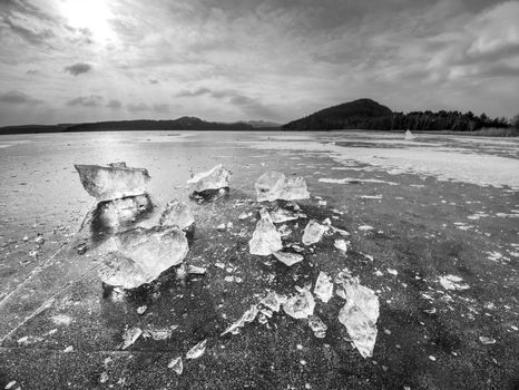 Ice fragments on frozen lake water level. The ice broken into shinning jagged pieces.  Dark natural backlight