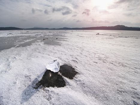 Drifting piece of iceberg and sun glaring on thick ice cover.  Drifting ice floes on  river.