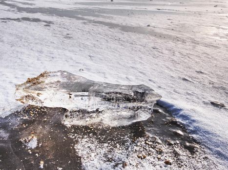 Blue ice of frozen sea and small ice fragments. Hilly island at far horizon. Winter silent in bay. 