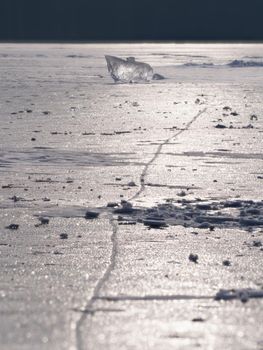 Abstract ice floe on frozen lake. Weathered ice and sparkling of evening sun. Deep ice cracks.