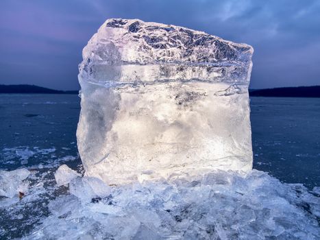 Arctic ice. A large piece of natural ice on a green blue flat ice of frozen lake, water bubbles texture. Shiny detail inside wonderful of transparent. stalactite ice.