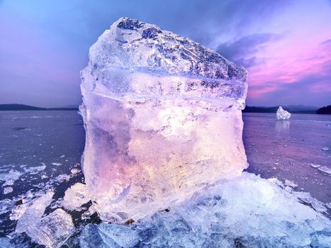 Melting pieces of chopped ice blocks. Strong colorful backlight shine deep cracks, low angle view. Far flat horizon.