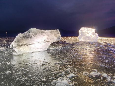 Shining wrinkled surface broken ice, fresh icy pieces on flat frost ground. Colorful winter sunset.