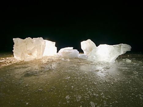 Blue ice cubes shine on flat glacier surface.  Thanks to spot light shine curved details inside of ice, frozen bubbles and scratches.