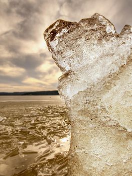 Heap of shining ice on beach.  Ice in a bay overlaid by night strong wind. Muddy beach with yellow brown icy floes