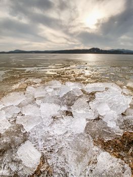 Heap of shining ice on beach.  Ice in a bay overlaid by night strong wind. Muddy beach with yellow brown icy floes