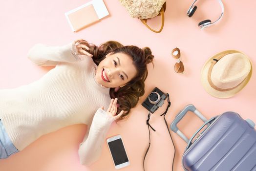 Beauty Asian girl lying on pink floor with all travel luggage around her. Top view.