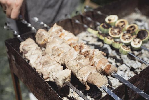 Backyard barbecue. Mans hands grilling kebab on metal skewer fresh meat.