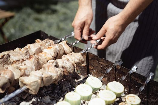 Backyard barbecue. Mans hands grilling kebab on metal skewer fresh meat.