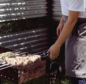 Backyard barbecue. Mans hands grilling kebab and vegetables on metal skewers.