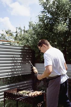 Backyard barbecue. Mans hands grilling kebab and vegetables on metal skewers.