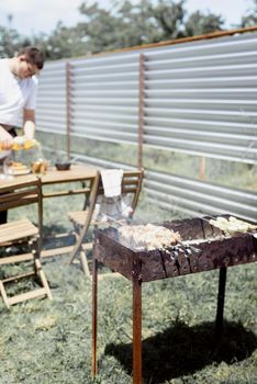 Backyard barbecue. Mans hands grilling kebab and vegetables on metal skewers. Young man grilling kebabs on skewers. Charcoal grill outdoors with meat grilled