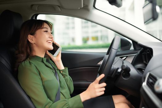 cheerful young woman driving a car and talking on the smartphone