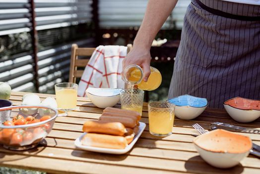 Young man preaparing table for picnic , holding bottle with lemonade in sunny summer afternoon. Backyard barbecue