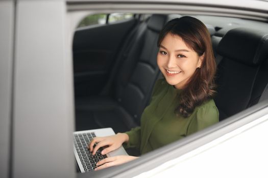 Beautiful businesswoman using laptop while sitting on a backseat of a car.