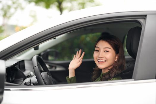 Hello! Beautiful young cheerful woman looking at camera with smile and waving while sitting in her car