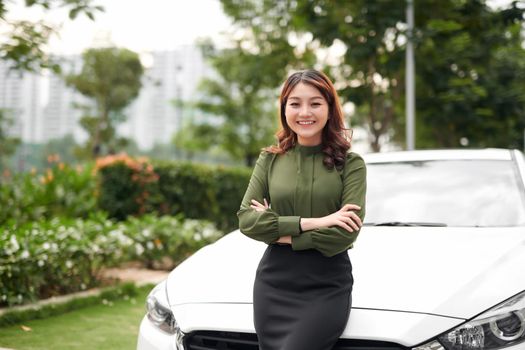 Happy woman with crossed arms standing by her car