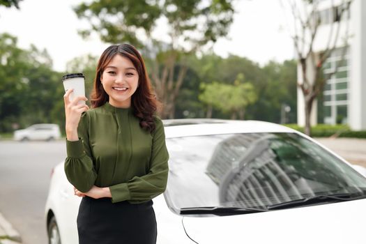 Portrait of smiling sexy woman drinking mug of beverage while standing near car outside